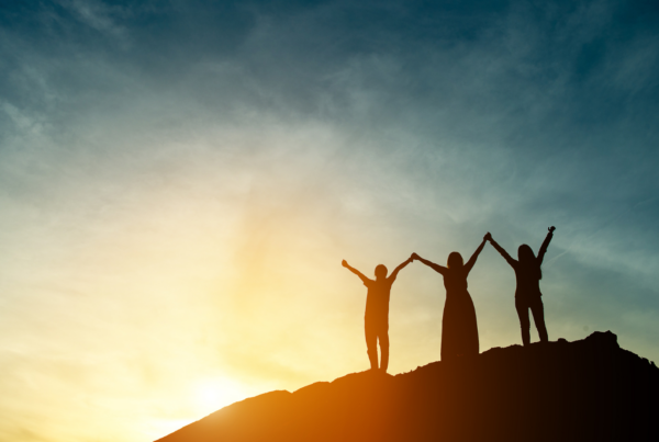 women on mountain with hands in the air